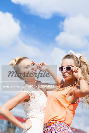 two young girls in summer outfit pose for the camera against the blue sky