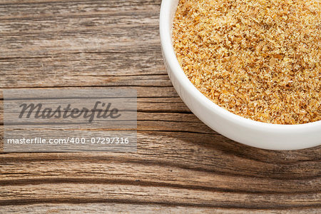golden flaxseed meal - a ceramic bowl on grained wood background
