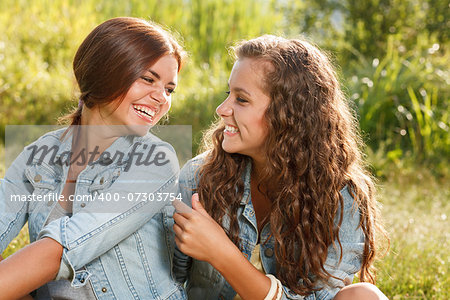 two girlfriends in jeans wear outdoors sitting  having fun looking at each other