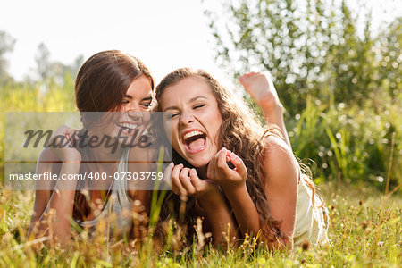 two girlfriends in T-shirts  lying down on grass laughing having good time