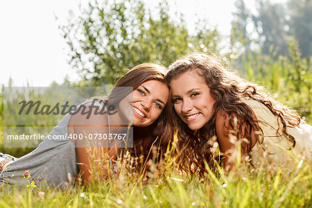 two girlfriends wearing T-shirts lying down on grass smiling looking at camera