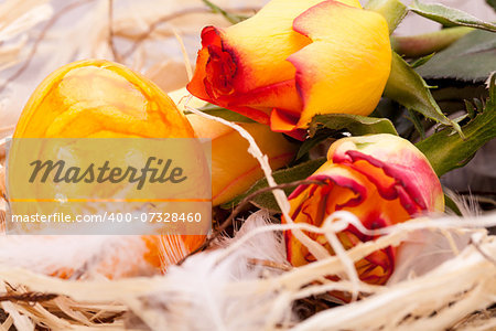 Vivid orange Easter egg with a painted marble pattern nestling in a straw nest with a fresh gerbera daisy and rose to celebrate Easter and spring