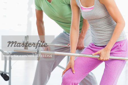 Mid section of fit young man and woman holding barbells in the gym