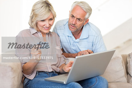 Casual mature couple doing online shopping through computer and credit card at home