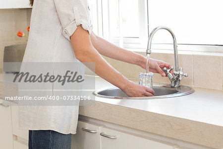 Side view mid section of a woman washing glass at washbasin in the kitchen at home