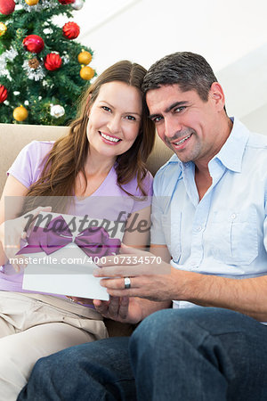 Portrait of loving couple holding Christmas present at home