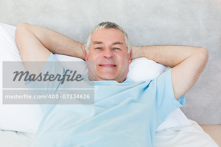 Portrait of senior man with hands behind head lying in bed