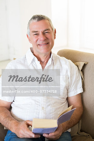 Portrait of smiling senior man holding book on sofa at home