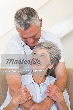 Senior man hugging wife sitting on sofa at home