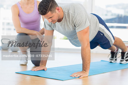 Female trainer assisting man with push ups at gym