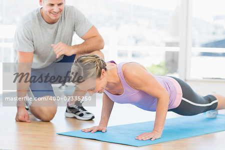 Male trainer assisting woman with push ups in fitness studio