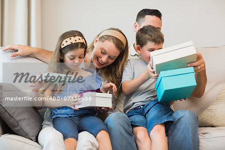 Happy family opening gifts while sitting on sofa at home