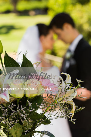 Close-up of bouquet with blurred newlywed couple in background at the park