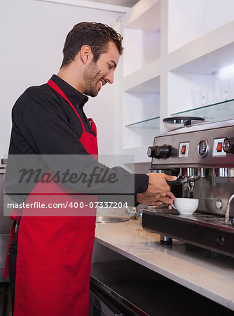 Happy young barista making cup of coffee in a cafe