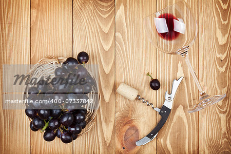 Red wine glass, corkscrew and grape on wooden table background