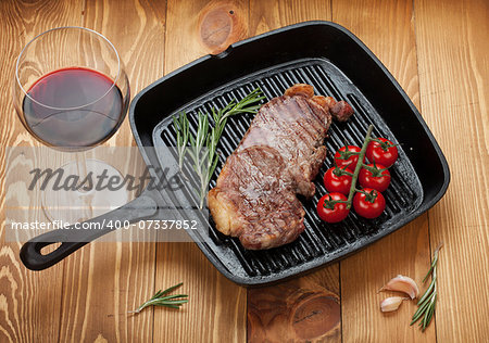 Sirloin steak with rosemary and cherry tomatoes on a frying pan with glass of wine