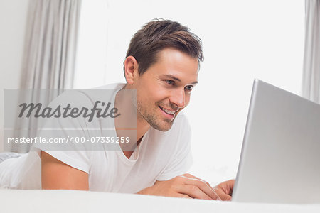 Relaxed casual young man using laptop in bed at home