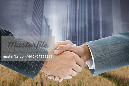 Composite image of business handshake against cityscape projection over yellow fields