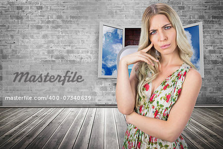 Frowning pretty blonde wearing flowered dress posing against window frame on red brick wall