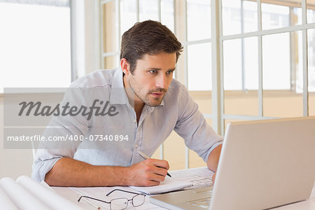 Concentrated young businessman working on blueprints and laptop in the office