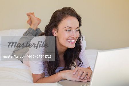 Full length of young woman using laptop while lying in bed at home