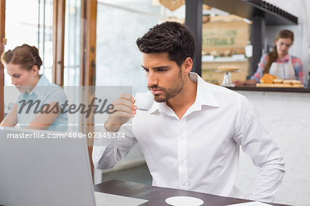 Concentrated young man drinking coffee while using laptop in the coffee shop