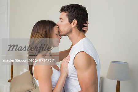 Side view of a loving young man kissing woman on forehead at home