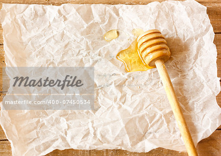 Wooden honey dipper with honey on a crumpled paper with copy space for text.