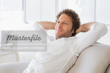 Relaxed well dressed man sitting with hands behind head on sofa in the house