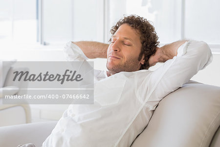 Relaxed well dressed man sitting with hands behind head on sofa in the house