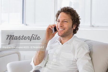 Smiling young man using mobile phone on sofa in the house