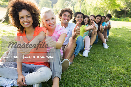 Portrait of confident university students gesturing thumbs up while sitting on campus