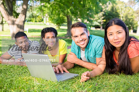 Portrait of smiling university students with laptop lying on grass on college campus