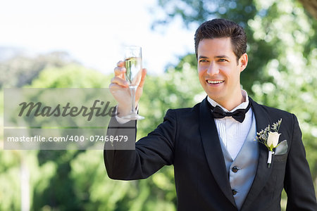 Happy young groom toasting champagne flute in garden