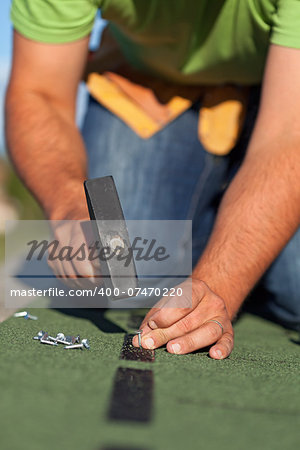 Man fastening the bitumen roof shingles - closeup on hands with hammer and nails