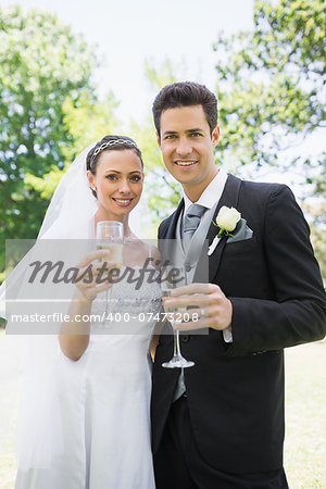 Portrait of bride and groom toasting champagne in park