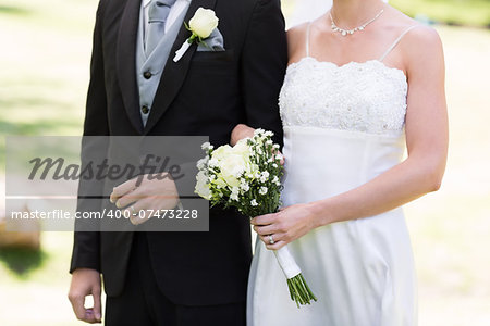 Mid section of newlywed couple holding hands in garden