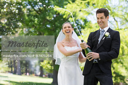 Young newlywed couple popping cork of champagne in park