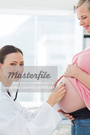 Portrait of beautiful doctor examining pregnant woman with stethoscope in clinic