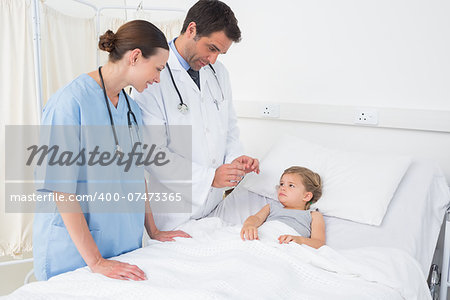 Doctors attending little girl lying in hospital bed