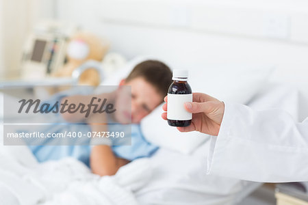 Closeup of doctor holding bottle of cough syrup with sick boy in hospital bed