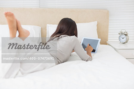 Young girl lying on bed using her tablet in her bedroom at home