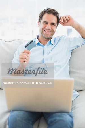 Cheerful man using laptop sitting on sofa shopping online at home in the living room