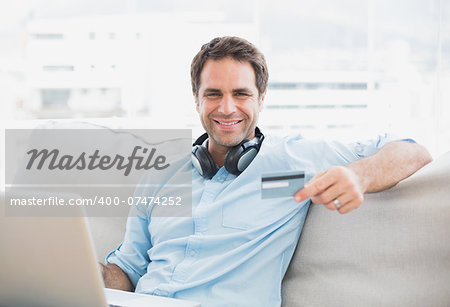 Happy handsome man sitting on sofa online shopping with laptop at home in the living room