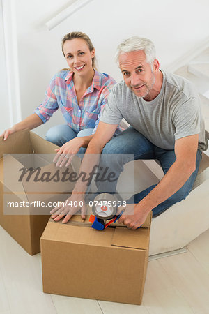 Happy couple sealing cardboard moving boxes in their old home