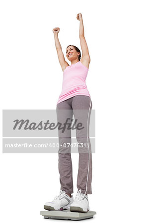 Low angle view of a young woman cheering on weight scale over white background