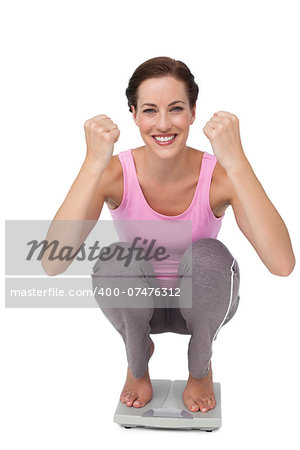 Portrait of a young woman cheering on weight scale over white background