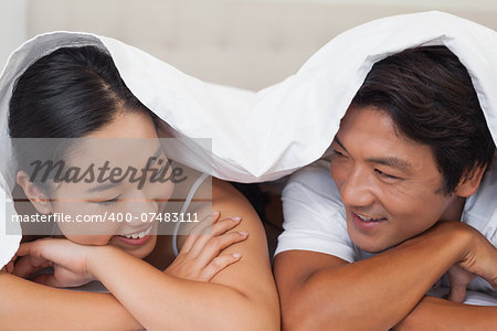 Happy couple lying on bed together under the duvet at home in bedroom