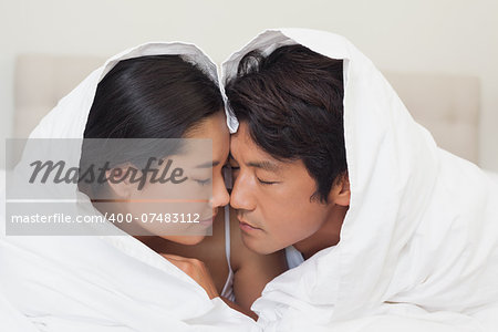 Happy couple lying on bed together under the duvet at home in bedroom