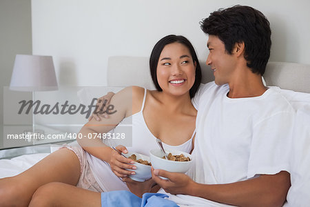 Happy couple having breakfast in bed at home in bedroom